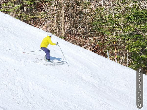 Skier in yellow jacket makes turn in soft spring snow