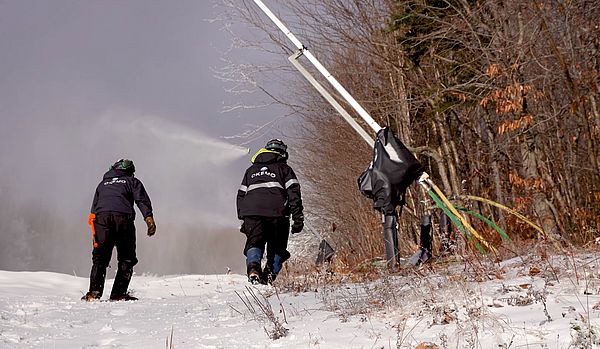 Two snowmakers with Okemo jackets walk uphill toward snowguns