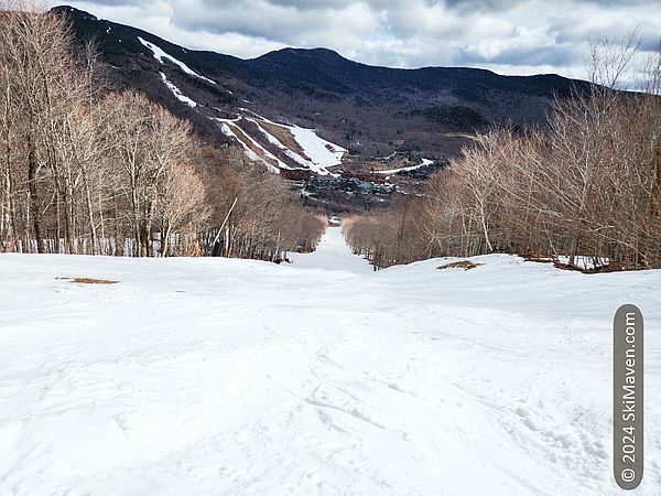 Looking down a straight bumpy ski trail with trails in view on other side of resort