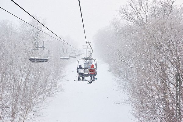 Photo of two snowboarders on a triple chairlift