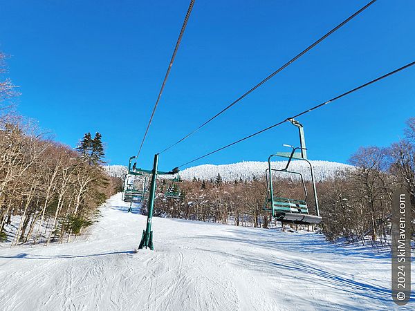 View from double chairlift with a broad ski slope and blue sky