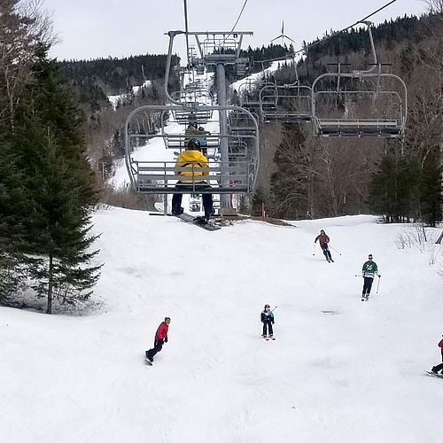 A group of skiers and riders comes down the hill under the Vista quad lift