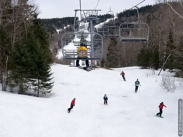 A group of skiers and riders comes down the hill under the Vista quad lift