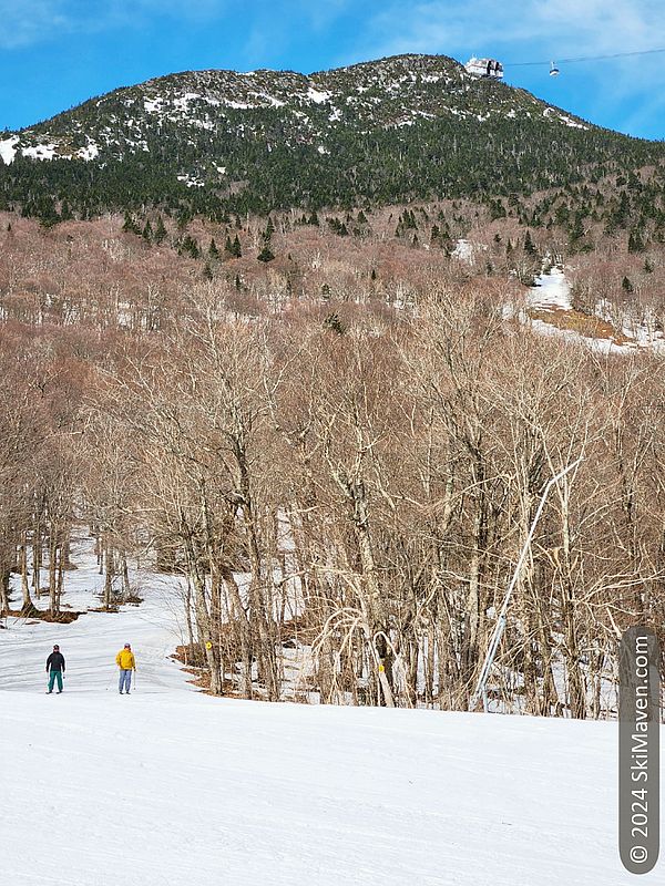 2 skiers in foreground and tram arriving at top in the background