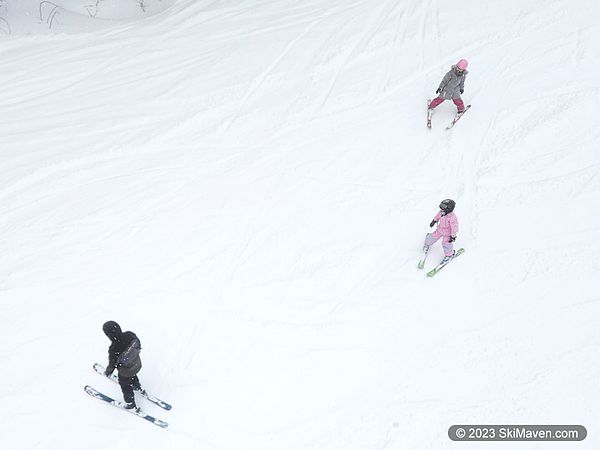 Instructor leads two small kids doing snowplow turns