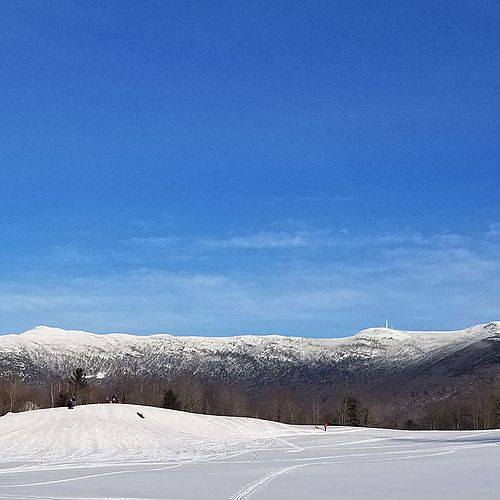 A snowy sledding hill with a big mountain in background