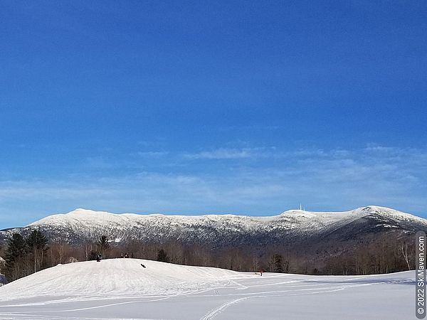 A snowy sledding hill with a big mountain in background