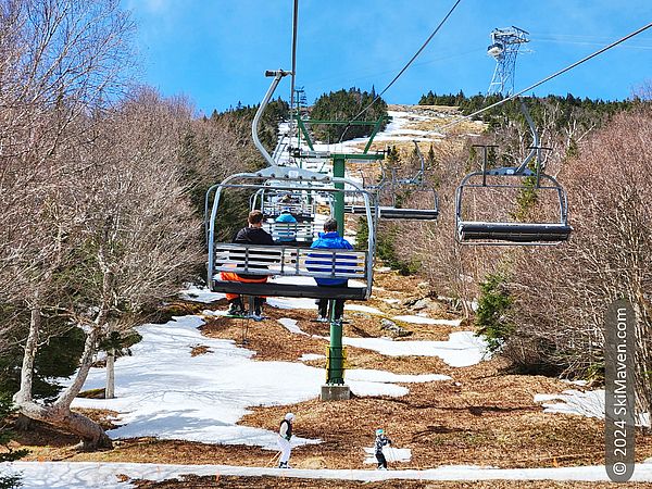 3 skiers ride a chairlift with two skiers passing underneath