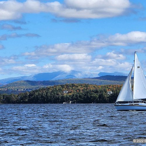 Snow atop Mt. Mansfield with a lake and sailboat in foreground