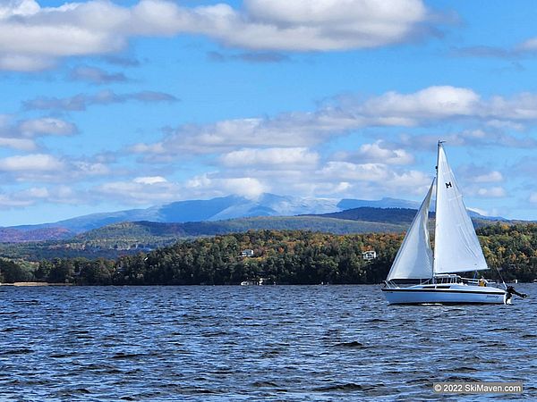 Snow atop Mt. Mansfield with a lake and sailboat in foreground