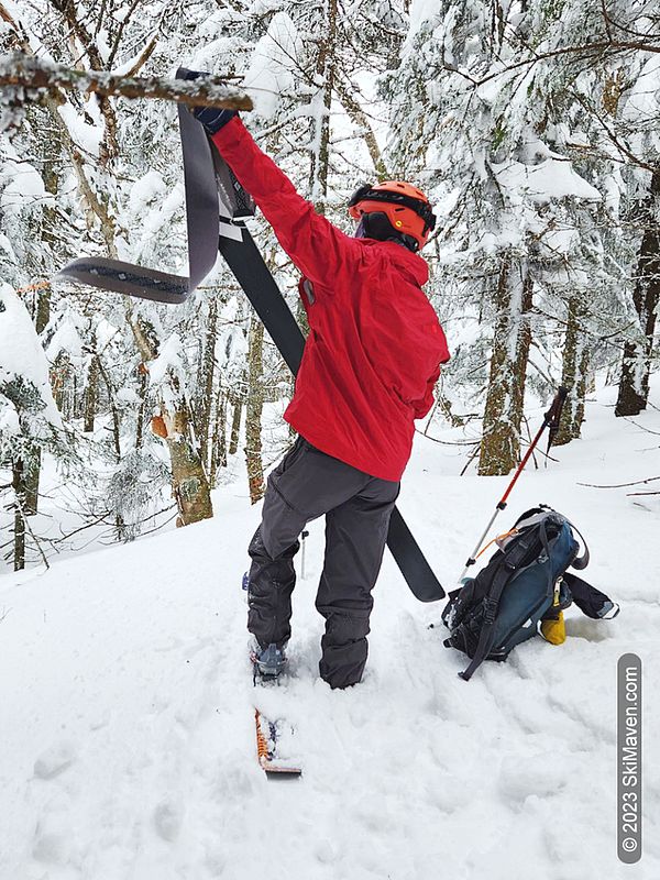A skier stands in snow and takes skins off his skis