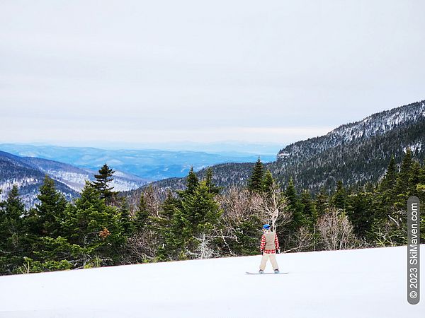 Snowboarder on a groomed slope with a mountain and lake view