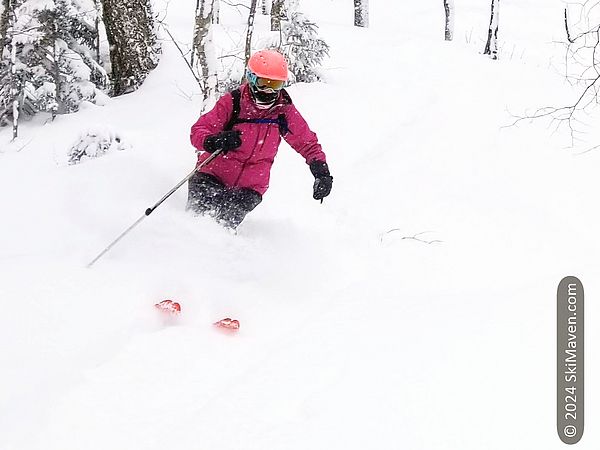 Skier in pink makes a turn in knee-deep powder