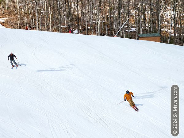 Two skiers make turns on a broad slope near the six-person lift