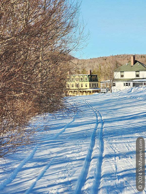 Classic ski tracks heading toward a white building and mustard-yellow building