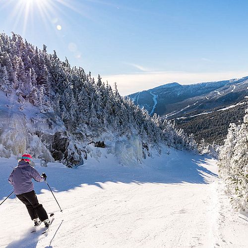 Photo of skier making turns at Smugglers' Notch in sunshine with mountain view