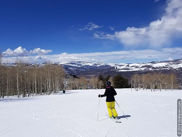 Skier makes turns at Arrowhead with aspen trees and mountains in view