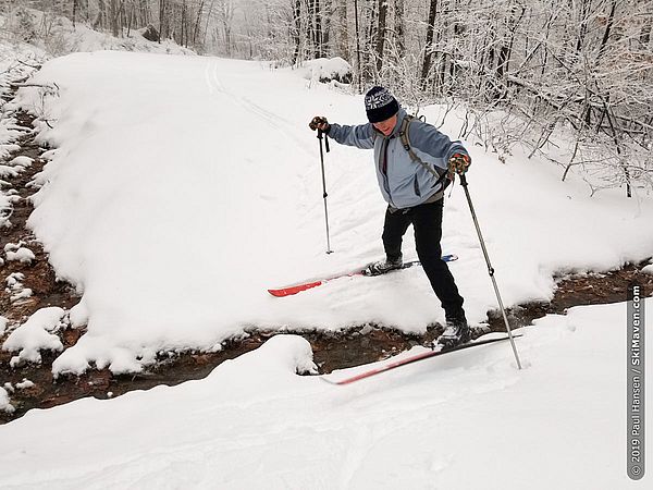 Photo of a Nordic skier jumping across a small stream