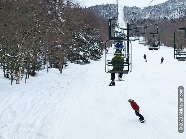 Skiers and riders descend under a double chairlift