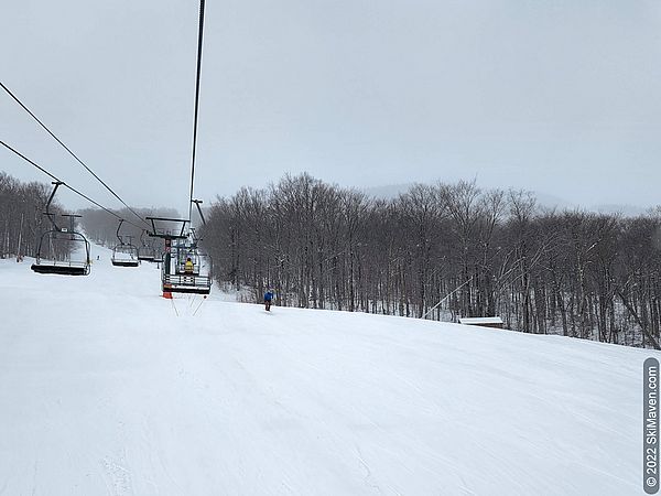 Photo of a chairlift with very few riders and a skier taking a jump