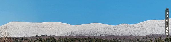 Panoramic view of snow-covered mountain range and blue sky