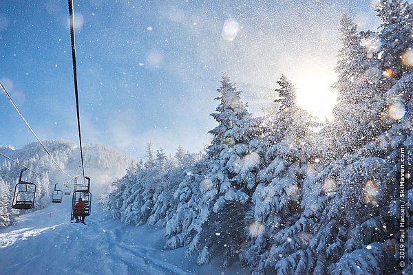 Photo of chairlift ascending a snowy Vermont mountain with small, sunlit snowflakes