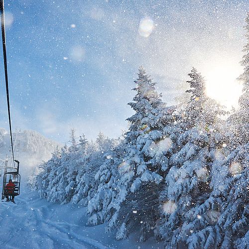 Photo of chairlift ascending a snowy Vermont mountain with small, sunlit snowflakes