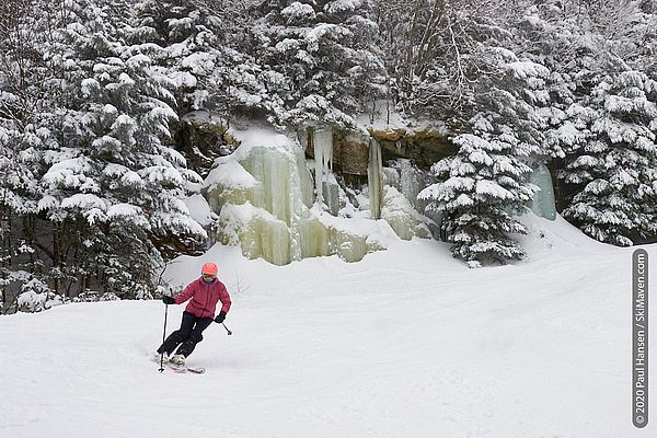 Photo of a skier turning in front of a frozen waterfall