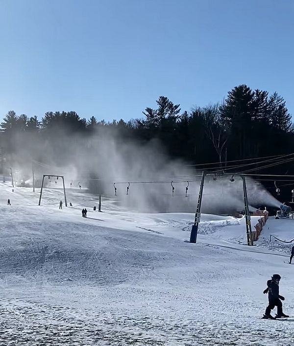Small ski hill with skiers and snowmaking in progress